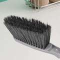 Woman using the long-handle cleaning brush for scrubbing a kitchen sink.