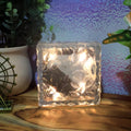 An ice cube solar light casting a soft glow on green foliage in a garden.