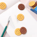 A child's hand holding a fun biscuit eraser next to a pencil, showing usage.