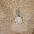 A white plastic measuring spoon demonstrating its use as a bag clip on a food bag.